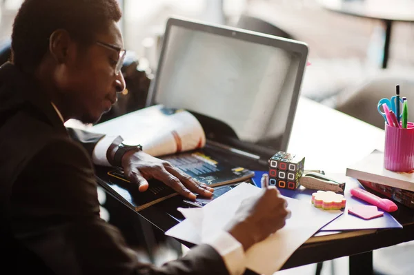 Business african american man wear on black suit and glasses sitting at office with laptop and working.