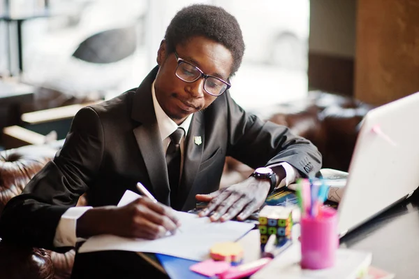 Business african american man wear on black suit and glasses sitting at office with laptop and working.