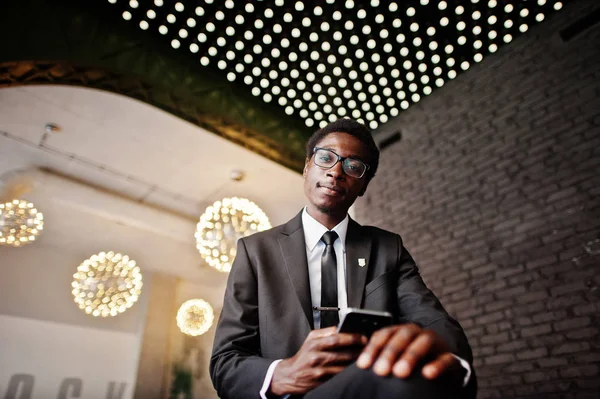 Business african american man wear on black suit and glasses at office looking on mobile phone against futuristic lights.