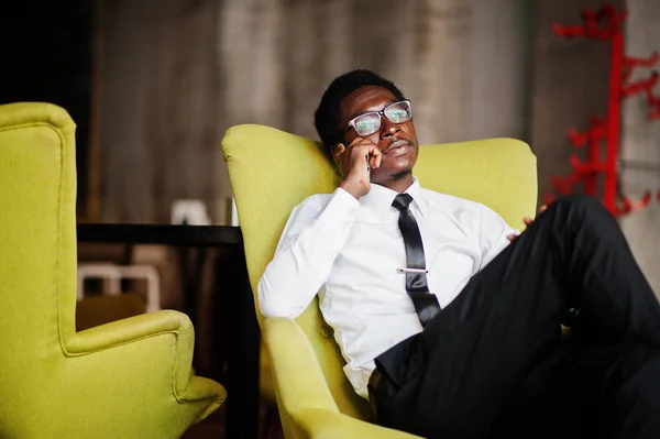 Business african american man wear on white shirt, tie and glasses at office, sitting on chair and speaking on phone.