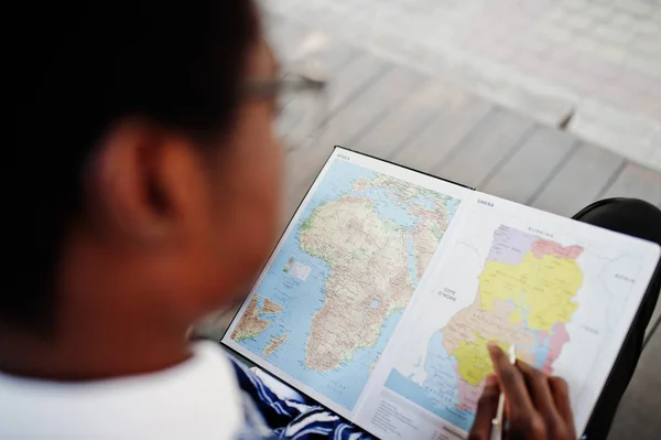African man in traditional clothes and glasses looking on map of Africa and Ghana at his notebook.