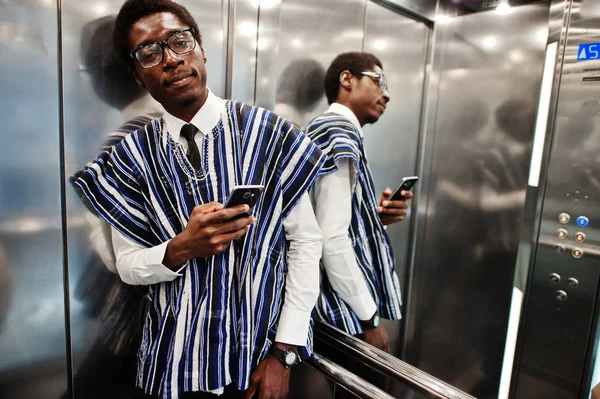 African man in traditional clothes and glasses with mobile phone at elavator or modern lift.