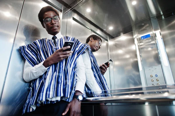 African man in traditional clothes and glasses with mobile phone at elavator or modern lift.
