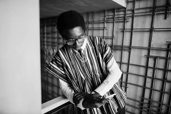 モダンな建物の屋内で提起された伝統的な服や手元の携帯電話でメガネでアフリカの実業家 — ストック写真