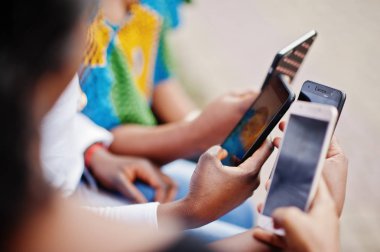 Grup dört Afro-Amerikan kız açık ve cep telefonları bakarak bankta oturmuş ellerini yukarıya kapatmak.