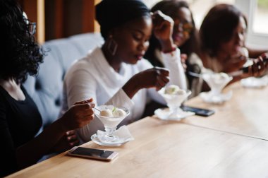 Kafede masada oturan ve buz yeme dört Afro-Amerikan kız tatlı krem.