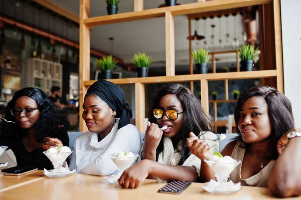 Four african american girls sitting on table at cafe and eating ice cream dessert.