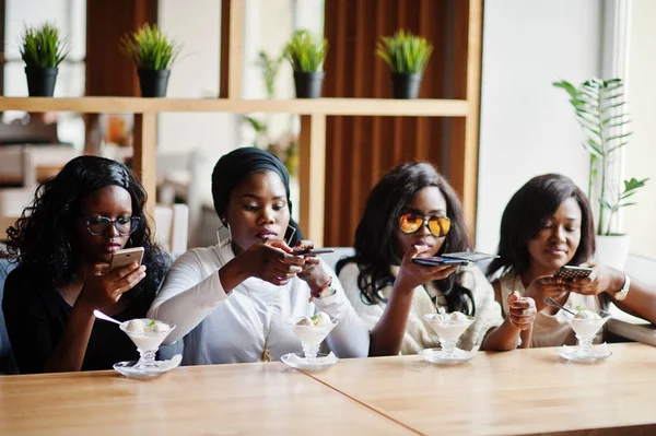 Four african american girls sitting on table at cafe with ice cream dessert and making food photo on phone.