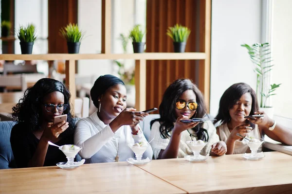 Four african american girls sitting on table at cafe with ice cream dessert and making food photo on phone.