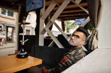 Arap adam gözlük ve askeri ceket sigara nargile sokak barında şık sakal. Geri kalan Arap modelinde.