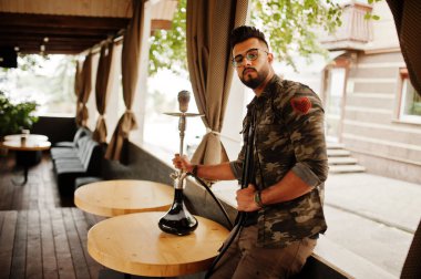 Arap adam gözlük ve askeri ceket sigara nargile sokak barında şık sakal. Geri kalan Arap modelinde.