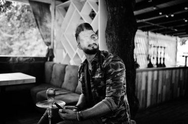 Arap adam gözlük ve askeri ceket sigara nargile sokak barında şık sakal. Geri kalan Arap modelinde.