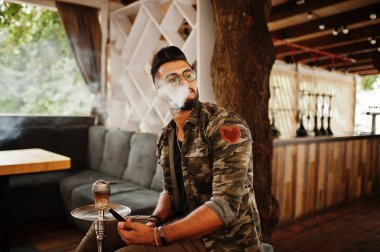 Arap adam gözlük ve askeri ceket sigara nargile sokak barında şık sakal. Geri kalan Arap modelinde.