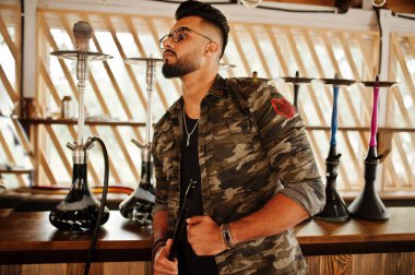 Arap adam gözlük ve askeri ceket sigara nargile sokak barında şık sakal. Geri kalan Arap modelinde.