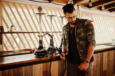 Arap adam gözlük ve askeri ceket sigara nargile sokak barında şık sakal. Geri kalan Arap modelinde.