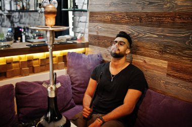 Arap adam gözlük ve siyah tişört sigara nargile bar kapalı şık sakal. Geri kalan Arap modelinde.