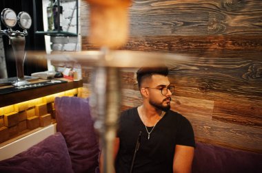 Arap adam gözlük ve siyah tişört sigara nargile bar kapalı şık sakal. Geri kalan Arap modelinde.