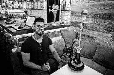 Arap adam gözlük ve siyah tişört sigara nargile bar kapalı şık sakal. Geri kalan Arap modelinde.