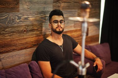 Arap adam gözlük ve siyah tişört sigara nargile bar kapalı şık sakal. Geri kalan Arap modelinde.
