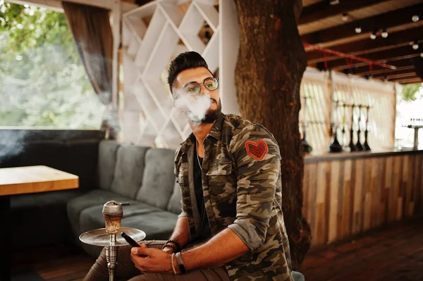 Arap adam gözlük ve askeri ceket sigara nargile sokak barında şık sakal. Geri kalan Arap modelinde.