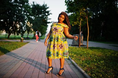 Sevimli küçük yükseklik Afro-Amerikan Kız dreadlocks, günbatımında poz renkli sarı elbise giymek.