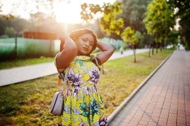 Sevimli küçük yükseklik Afro-Amerikan Kız dreadlocks, günbatımında poz renkli sarı elbise giymek.