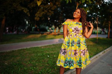 Sevimli küçük yükseklik Afro-Amerikan Kız dreadlocks, günbatımında poz renkli sarı elbise giymek.