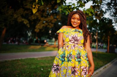 Sevimli küçük yükseklik Afro-Amerikan Kız dreadlocks, günbatımında poz renkli sarı elbise giymek.