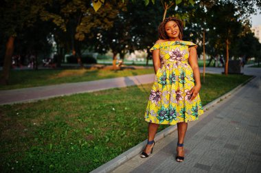 Sevimli küçük yükseklik Afro-Amerikan Kız dreadlocks, günbatımında poz renkli sarı elbise giymek.