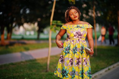 Sevimli küçük yükseklik Afro-Amerikan Kız dreadlocks, günbatımında poz renkli sarı elbise giymek.