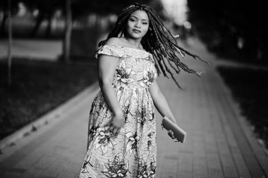 Sevimli küçük yükseklik Afro-Amerikan Kız dreadlocks, günbatımında poz renkli sarı elbise giymek. Siyah ve beyaz.