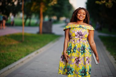 Sevimli küçük yükseklik Afro-Amerikan Kız dreadlocks, günbatımında poz renkli sarı elbise giymek.