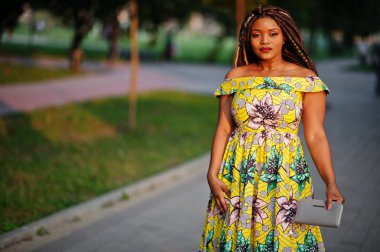 Sevimli küçük yükseklik Afro-Amerikan Kız dreadlocks, günbatımında poz renkli sarı elbise giymek.