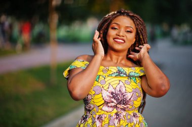 Sevimli küçük yükseklik Afro-Amerikan Kız dreadlocks, günbatımında poz renkli sarı elbise giymek.