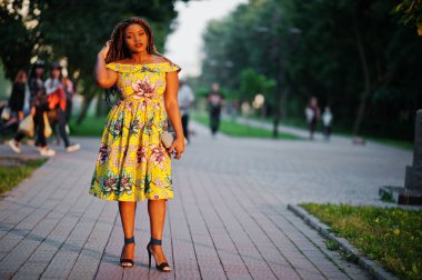 Sevimli küçük yükseklik Afro-Amerikan Kız dreadlocks, günbatımında poz renkli sarı elbise giymek.