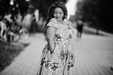 Sevimli küçük yükseklik Afro-Amerikan Kız dreadlocks, günbatımında poz renkli sarı elbise giymek. Siyah ve beyaz.