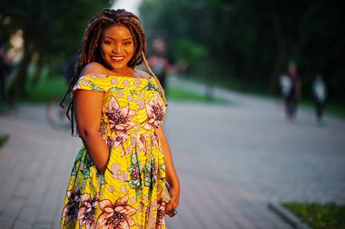 Sevimli küçük yükseklik Afro-Amerikan Kız dreadlocks, günbatımında poz renkli sarı elbise giymek.