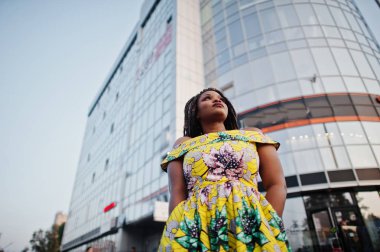 Sevimli küçük yükseklik Afro-Amerikan Kız dreadlocks, bina büyük pencereler karşı yöneltilen renkli sarı elbise giymek.