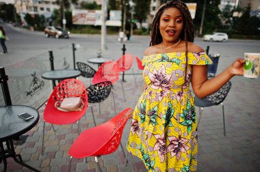 Sevimli küçük yükseklik Afro-Amerikan Kız dreadlocks, kahve ile açık kafe poz renkli sarı elbise giymek.