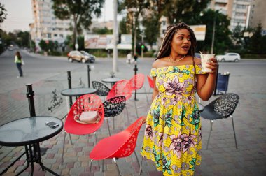 Sevimli küçük yükseklik Afro-Amerikan Kız dreadlocks, kahve ile açık kafe poz renkli sarı elbise giymek.