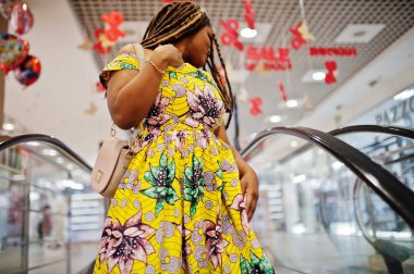 Sevimli küçük yükseklik Afro-Amerikan Kız dreadlocks, alışveriş merkezi yürüyen ayakta renkli sarı elbise giymek.