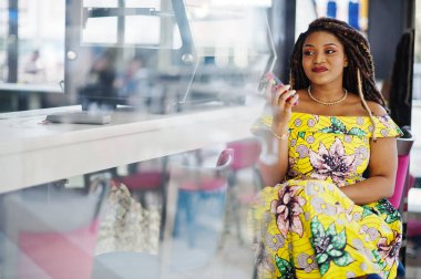 Sevimli küçük yükseklik Afro-Amerikan Kız dreadlocks, Alışveriş Merkezi kafede oturan ve konuşan renkli sarı elbise giymek.