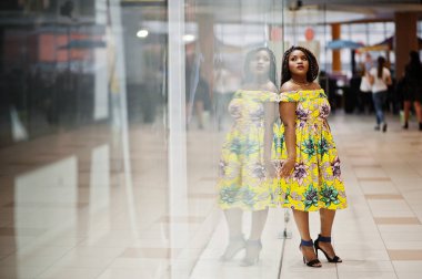 Sevimli küçük yükseklik dreadlocks, Afrikalı-Amerikalı kızla dükkanı Vitrini Ticaret Merkezi poz renkli sarı elbise giymek.