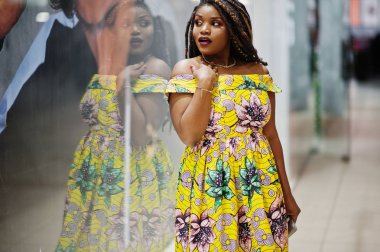 Sevimli küçük yükseklik dreadlocks, Afrikalı-Amerikalı kızla dükkanı Vitrini Ticaret Merkezi poz renkli sarı elbise giymek.