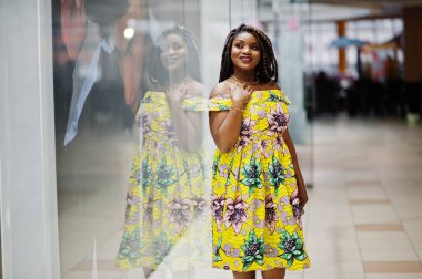 Sevimli küçük yükseklik dreadlocks, Afrikalı-Amerikalı kızla dükkanı Vitrini Ticaret Merkezi poz renkli sarı elbise giymek.