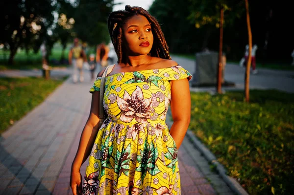 Sevimli küçük yükseklik Afro-Amerikan Kız dreadlocks, günbatımında poz renkli sarı elbise giymek.