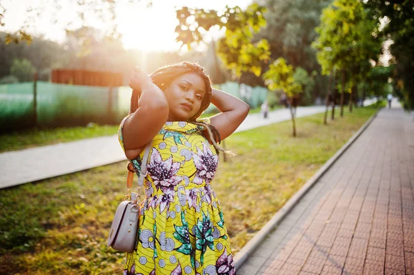 Sevimli küçük yükseklik Afro-Amerikan Kız dreadlocks, günbatımında poz renkli sarı elbise giymek.