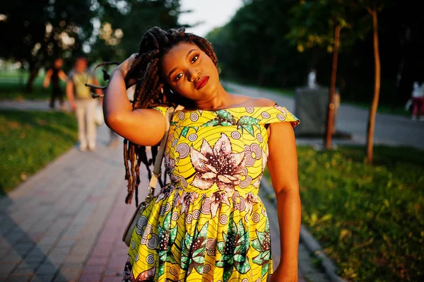 Sevimli küçük yükseklik Afro-Amerikan Kız dreadlocks, günbatımında poz renkli sarı elbise giymek.