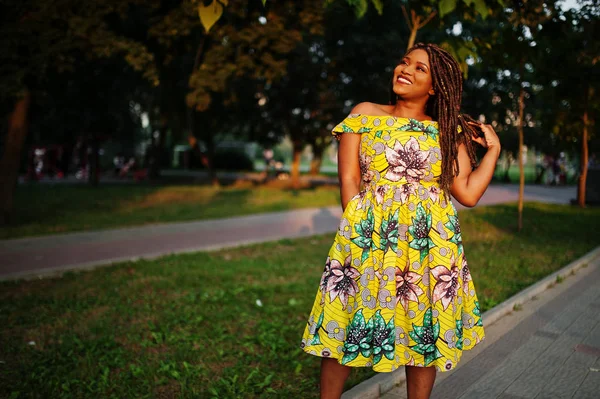 Sevimli küçük yükseklik Afro-Amerikan Kız dreadlocks, günbatımında poz renkli sarı elbise giymek.