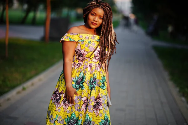 Sevimli küçük yükseklik Afro-Amerikan Kız dreadlocks, günbatımında poz renkli sarı elbise giymek.
